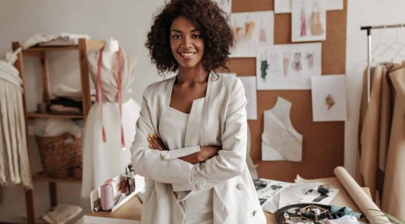 beautiful-curly-brunette-dark-skinned-fashion-designer-poses-office-leans-table